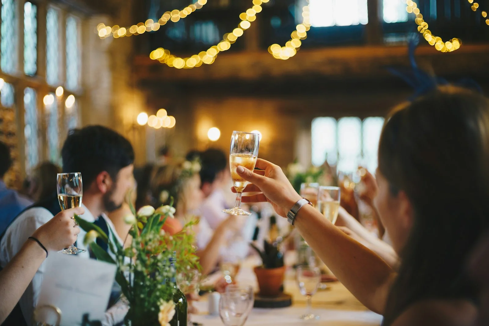 Goście weselni wznoszący toast przy świetle lampek